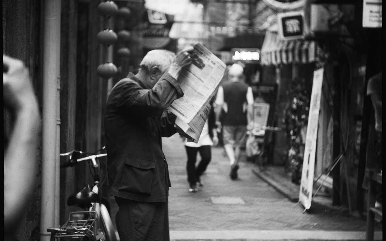 black and white image of man reading newspaper in the street