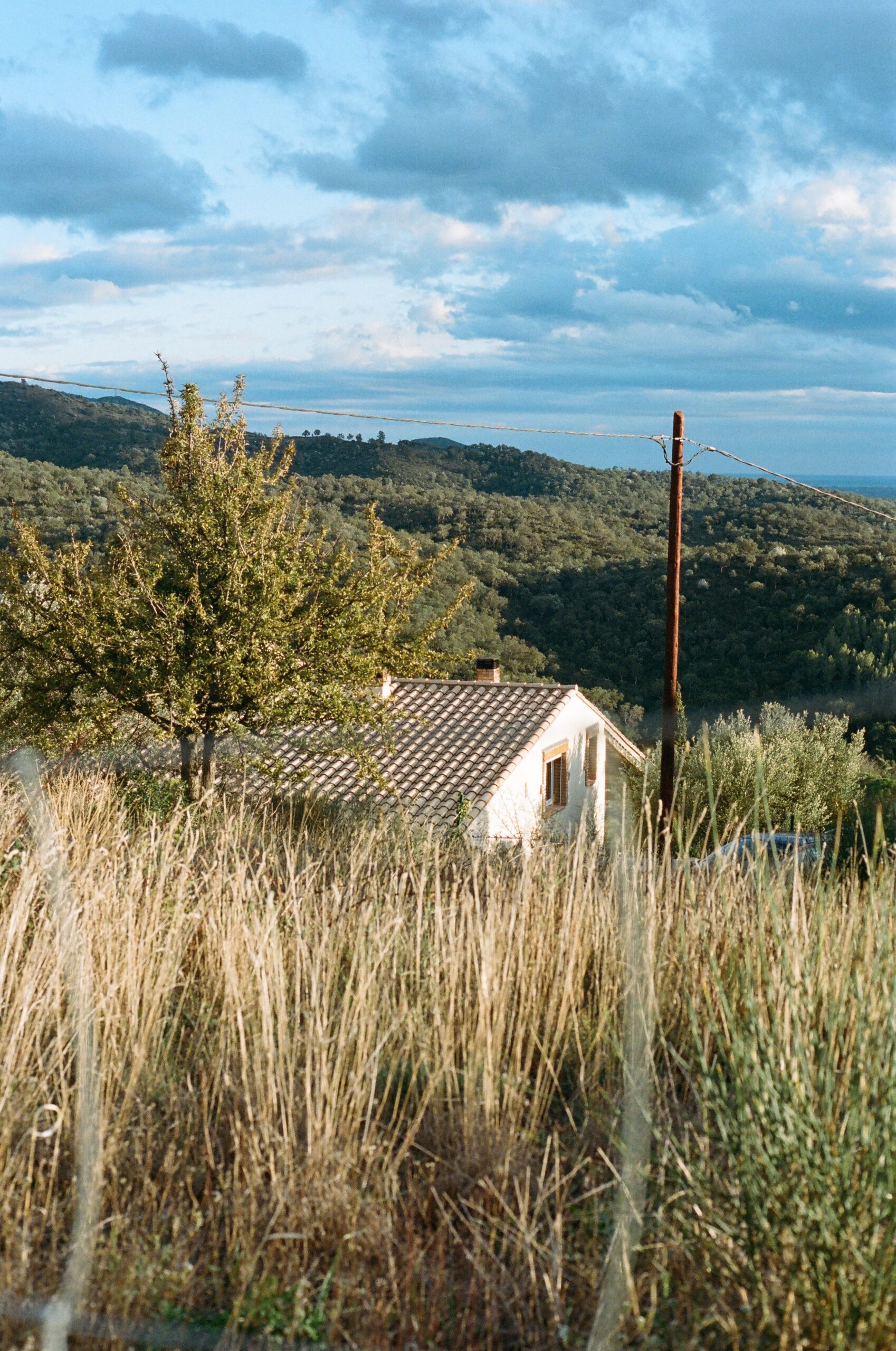 A photo of a house in a grassy area, with hills and a blue sky in the background